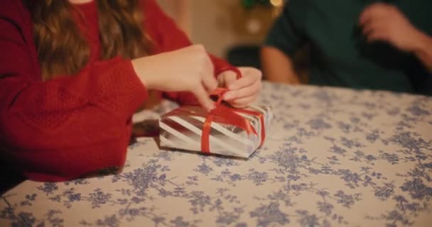 Sezione centrale della donna che lega il nastro sulla scatola regalo seduta da un amico maschio a tavola durante il Natale - Filmati, video