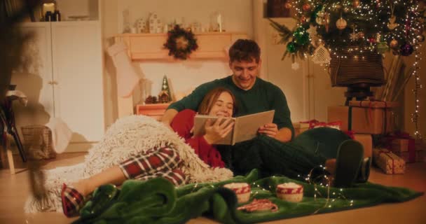 Улыбающаяся женщина разговаривает во время просмотра фотоальбома с другом в гостиной во время Рождества - Кадры, видео
