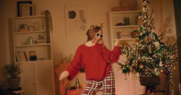 Güneş gözlüğü takan genç bir kadın Noel boyunca evde dans ederken eğleniyor. - Video, Çekim