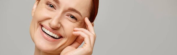 banner of cheerful and redhead woman looking at camera on grey background, healthy smile - Photo, Image