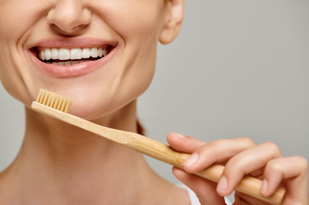 ostříhaný záběr šťastné ženy ve třiceti s bílými zdravými zuby držící bambusový kartáček na zuby, zubní péče - Fotografie, Obrázek
