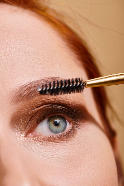 abgeschnittene Ansicht einer Frau mit grünen Augen, die Mascara auf beigem Hintergrund aufträgt, Make-up und Schönheit - Foto, Bild