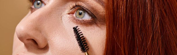 cropped banner of woman with green eyes applying mascara on beige background, makeup routine - Photo, Image