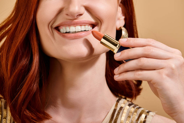 osittainen näkymä nainen hymyilee ja soveltamalla alaston huulipuna beige tausta, meikki tuote - Valokuva, kuva