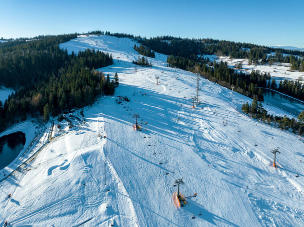 Pista de esquí, telesillas, esquiadores y snowboarders en Bialka Tatrzanska estación de esquí en Polonia en la montaña Kotelnica en invierno. Vista aérea con poca luz de diciembre - Foto, imagen