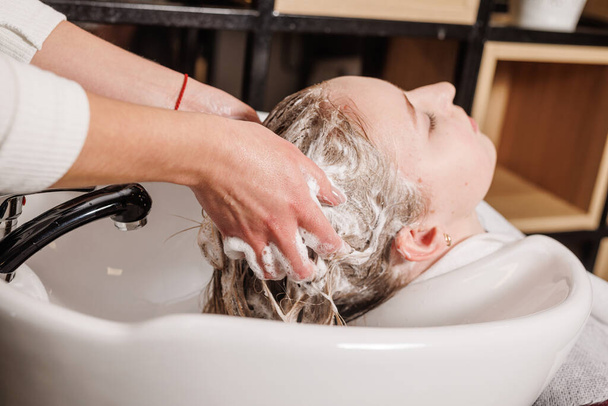 um mestre em um salão de beleza lava o cabelo de um cliente com xampu para cuidados com o cabelo em um salão de beleza - Foto, Imagem