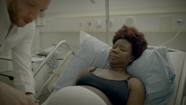 Νεαρή Αφρικανή με σγουρά μαλλιά ξαπλωμένη σε κρεβάτι Κλινικής Μιλώντας με γιατρό - Πλάνα, βίντεο