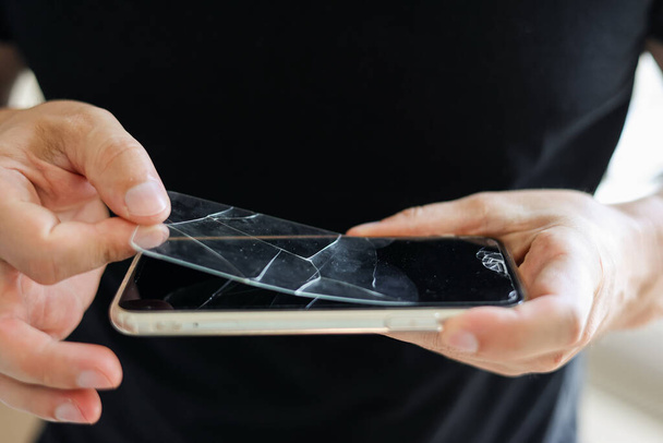 O reparador irreconhecível do processo está removendo o protetor de tela de vidro temperado quebrado e antigo do smartphone, vista de perto. Serviços de colagem e substituição de vidros de protecção danificados - Foto, Imagem