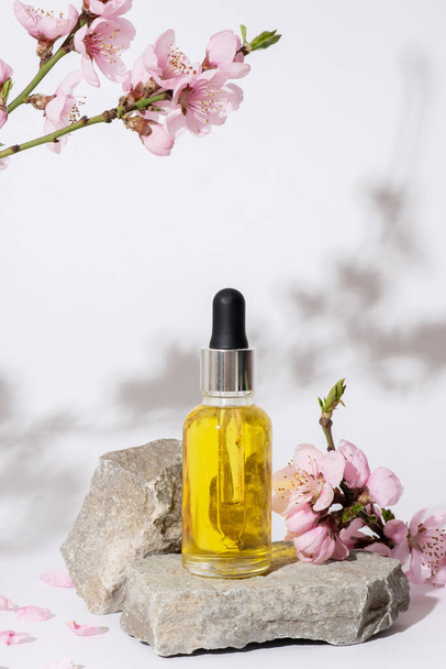 Cseresznyevirággal díszített palack olajjal a dobogón vagy talapzattal a természetből származó kőből. - Fotó, kép