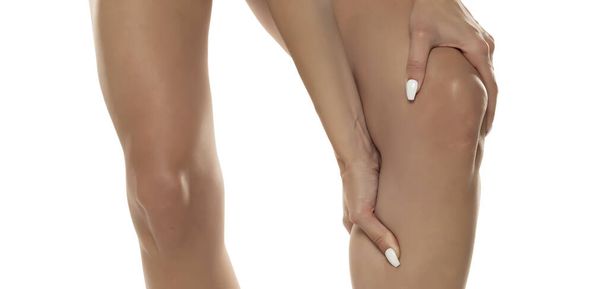 Жінка тримає коліно в явному болю, зображуючи дискомфорт, який вона відчуває на білому фоні студії. Концепція фізичного лиха і дискомфорту. - Фото, зображення