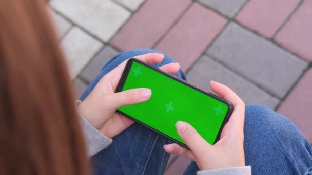 Klucz Chroma na zielonym ekranie smartfona z bliska. Nastolatka używa smartfona na zewnątrz, wpisując wiadomość lub grając. - Materiał filmowy, wideo