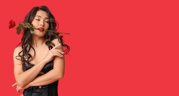 Sexy young woman in underwear and with rose in mouth on red background with space for text. Valentine's Day celebration - Photo, Image