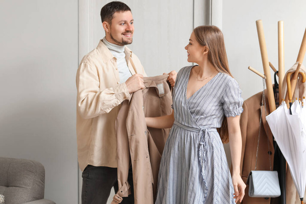 Young man putting coat on his wife at home - Foto, imagen