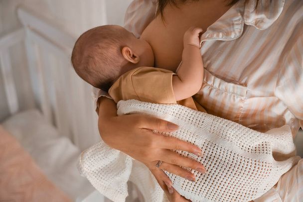 Mujer joven amamantando a su bebé en el dormitorio por la noche, primer plano - Foto, Imagen