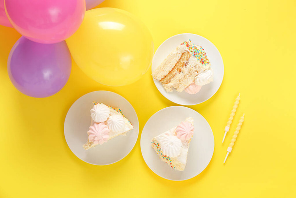 Globos y platos con trozos de delicioso pastel de cumpleaños sobre fondo amarillo - Foto, Imagen