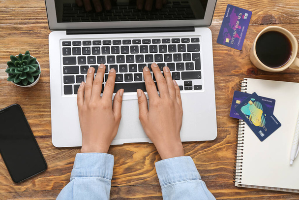 Женщина с ноутбуком и кредитными картами онлайн покупок на деревянном фоне - Фото, изображение