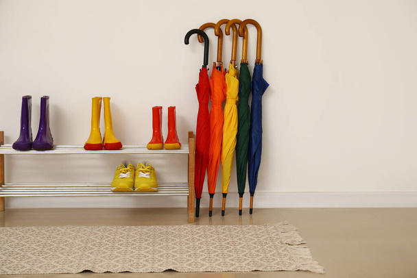 Βάση με διαφορετικά παπούτσια και πολύχρωμες ομπρέλες κοντά σε ανοιχτό τοίχο - Φωτογραφία, εικόνα