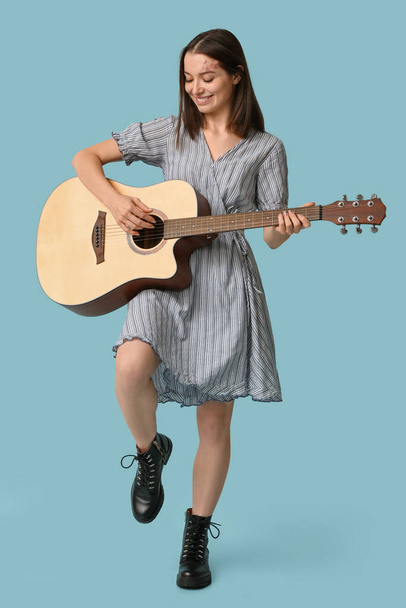 Гарненька молода жінка грає на акустичній гітарі на синьому фоні - Фото, зображення