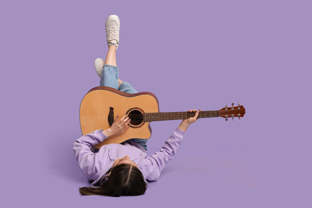 Mulher bonita tocando guitarra acústica enquanto deitada no fundo lilás - Foto, Imagem