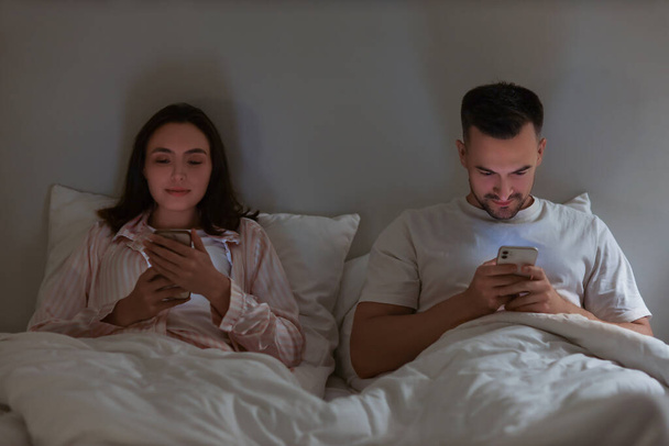 Geceleri yatak odasında cep telefonu kullanan genç bir çift. - Fotoğraf, Görsel