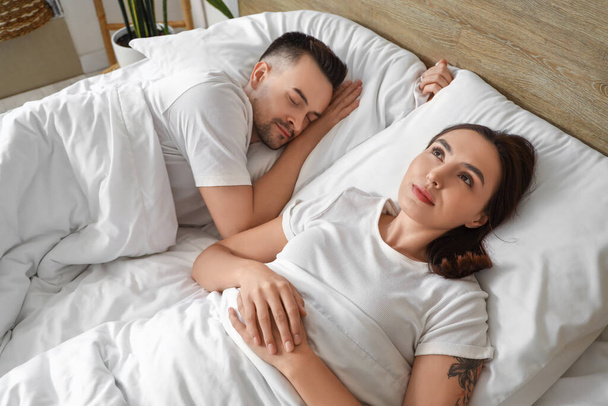 Awake young woman with her sleeping husband in bedroom - Photo, Image