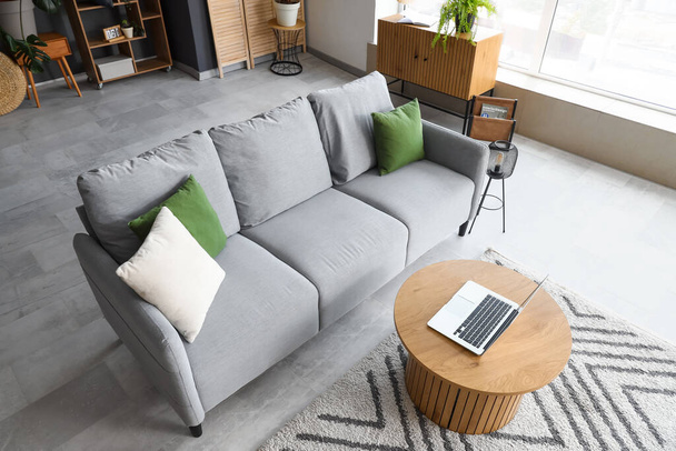 Інтер'єр сучасної вітальні з сірим диваном і ноутбуком на кавовому столі - Фото, зображення