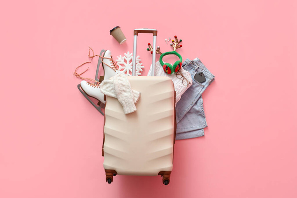 Valise avec vêtements chauds, patins à glace, cornes de cerf de Noël et tasse de café sur fond rose. Concept vacances d'hiver - Photo, image