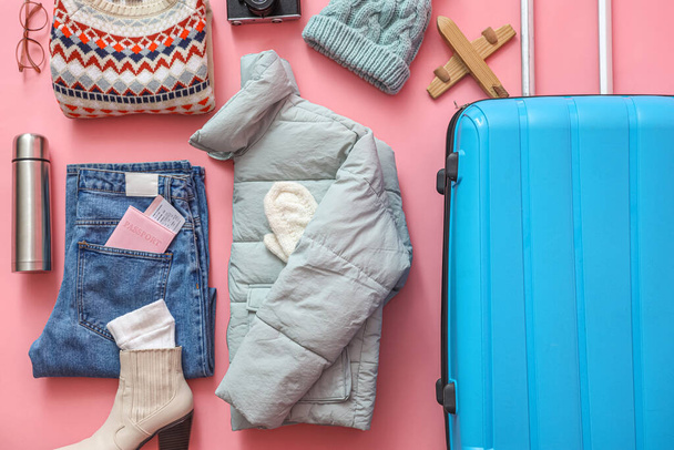 Suitcase with warm clothes, thermos and passport on pink background. Winter vacation concept - Photo, Image