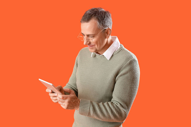 Uomo maturo in occhiali da vista utilizzando tablet computer su sfondo arancione - Foto, immagini