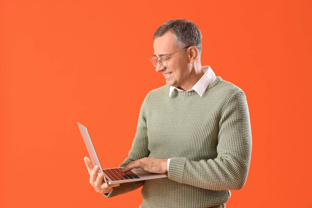 Hombre maduro en gafas con portátil sobre fondo naranja - Foto, Imagen