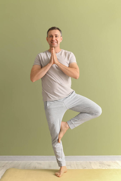 Homme mûr faisant du yoga sur tapis près du mur vert - Photo, image