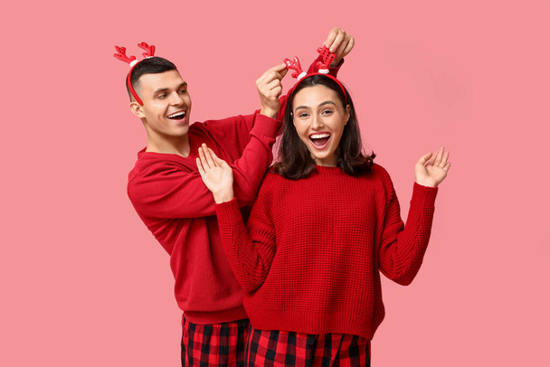 Glückliches junges Paar im Weihnachtsschlafanzug auf rosa Hintergrund - Foto, Bild