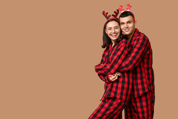 クリスマスのパジャマで幸せな若いカップルと鹿の反対者がベージュの背景に抱擁 - 写真・画像