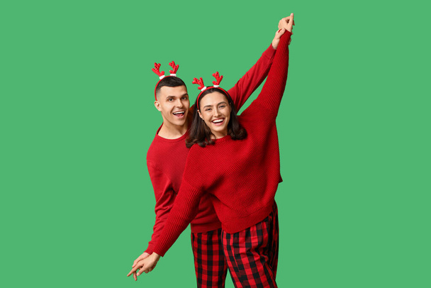 Happy young couple in Christmas pajamas on green background - Photo, Image