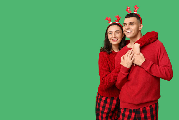 Happy young couple in Christmas pajamas hugging on green background - Photo, Image