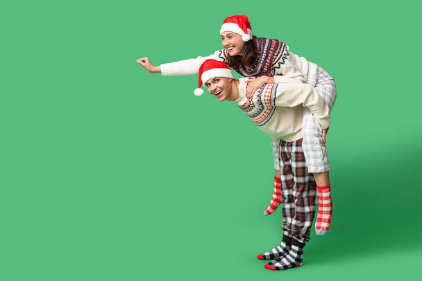 クリスマスのパジャマで幸せな若いカップルは緑の背景で楽しんでいます - 写真・画像