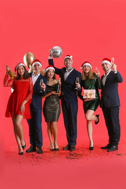 Grupo de jóvenes con champán y bola disco sobre fondo rojo. Celebración de Año Nuevo - Foto, imagen