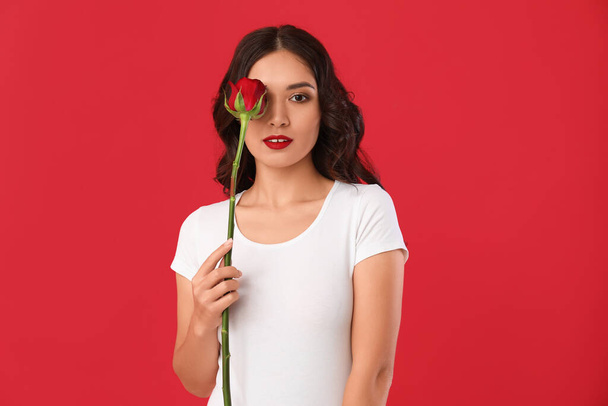 Νεαρή Ασιάτισσα με όμορφο τριαντάφυλλο σε κόκκινο φόντο - Φωτογραφία, εικόνα