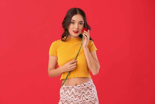 Young Asian woman with beautiful rose on red background - Photo, Image