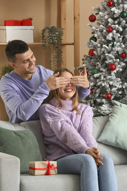 Hombre sorprendiendo a su novia en la sala de estar decorada para Navidad - Foto, Imagen