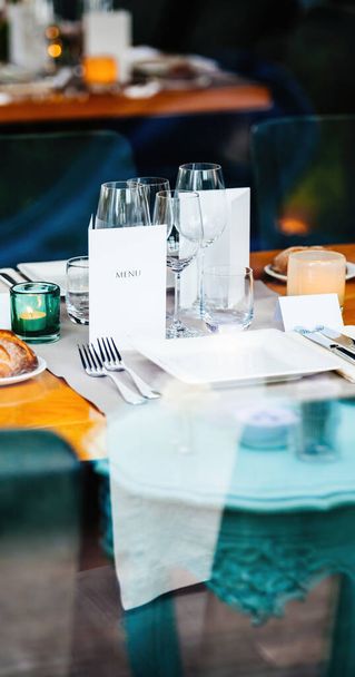 svatební hostina s textem menu zobrazeným na nedotčené bílé stránce, obklopená krásně zdobenými talíři, vidličkami a nádherným skleněným nádobím - Fotografie, Obrázek