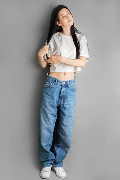 Beyaz tişörtlü ve kot pantolonlu genç bir kızın tam boy portresi.. - Fotoğraf, Görsel