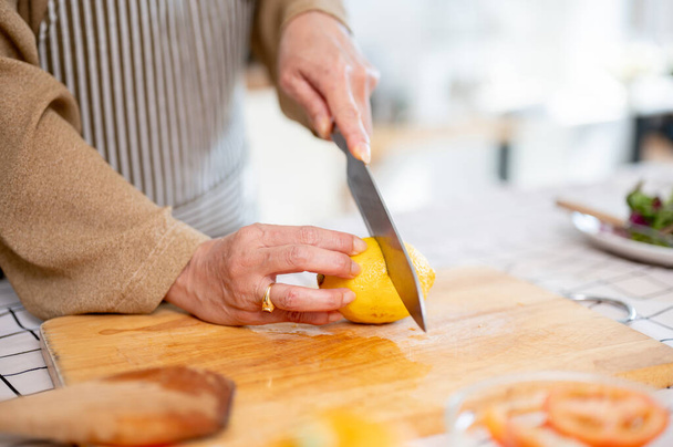 Imagen de cerca de una mujer cortando un limón, preparando ingredientes y cocinando en la cocina. Cocina casera, conceptos de personas y alimentos - Foto, imagen