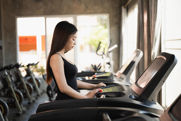 Asian athlete sport woman runner touch start button before workout running on treadmill in fitness club. Cardio workout. Healthy lifestyle, woman training in gym. Sport running concept. - Photo, Image