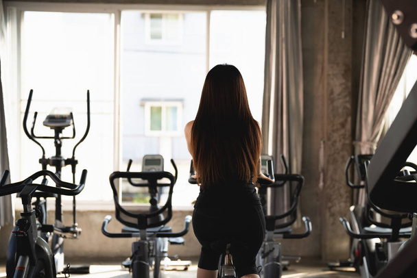 Zadní strana asijské sportovkyně cvičení na kole v tělocvičně, odhodlání kardio zhubnout, dělá ji zdravou. cvičení kolo žena fitness sportovní koncept. - Fotografie, Obrázek