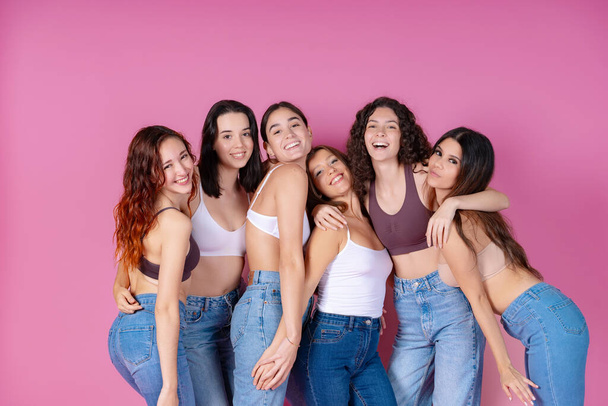 Kuusi hymyilevää naista omaksuu yhtenäisyyden ja kehon positiivisuuden näyttelyn, joka on asetettu iloiselle vaaleanpunaiselle taustalle. - Valokuva, kuva