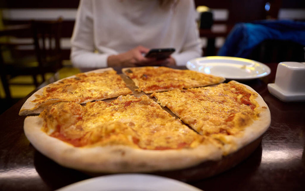 テーブルの上のピザのビューを閉じます. おいしい食事。 ピザ屋に集まった人々は,おいしいイタリア料理を楽しみながら楽しんでいます - 写真・画像