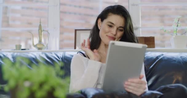 Woman, wave and tablet for video call at home, conversation and chatting online on couch. Happy female person, funny and comedy on technology or internet connection, streaming and humor or greeting. - Footage, Video