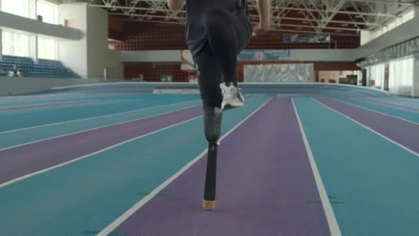 Tilt slow shot di corridore maschio caucasico determinato con disabilità utilizzando la lama protesica per allenarsi sullo stadio al coperto - Filmati, video