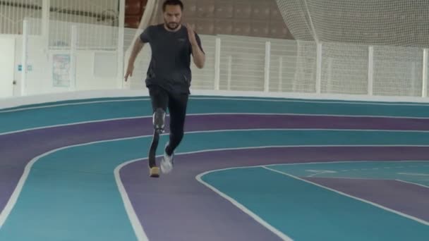 Slowmo de atleta masculino caucásico con la hoja de la extremidad protésica que funciona en pista en el estadio cubierto - Imágenes, Vídeo
